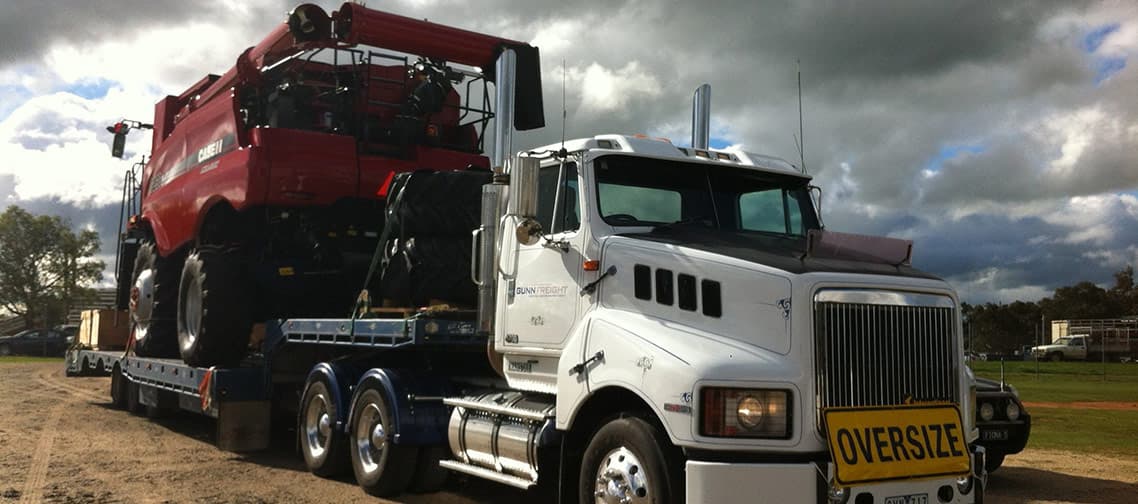 Low loader carrying farm machinery at dusk